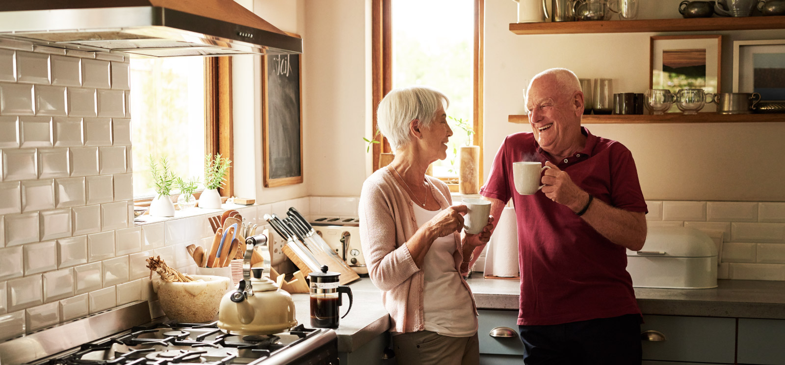 Mature couple enjoy coffee standing in kitchen.